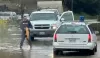 Man stapt uit zijn auto om een ​​vis te vangen op een overstroomde snelweg